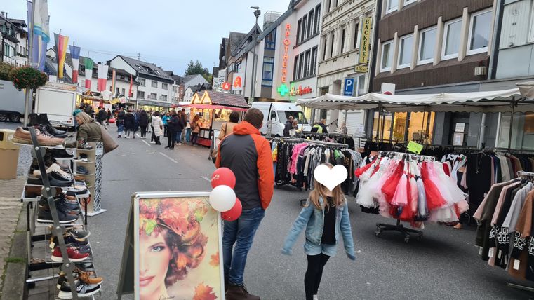 Eine lebhafte Marktstraße mit Ständen für Kleidung und Schuhe. Menschen schlendern durch die Verkaufsstände und genießen die Atmosphäre.