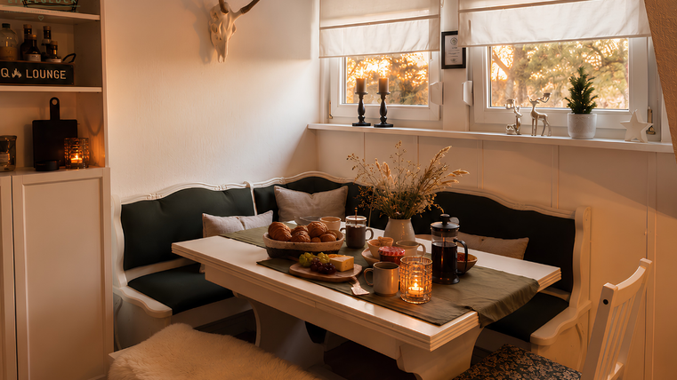 Ein gemütlicher Essbereich mit einem großen Tisch und modernen Stühlen. Auf dem Tisch liegt ein platter Brunch mit Snacks und Getränken, umgeben von warmem Licht.