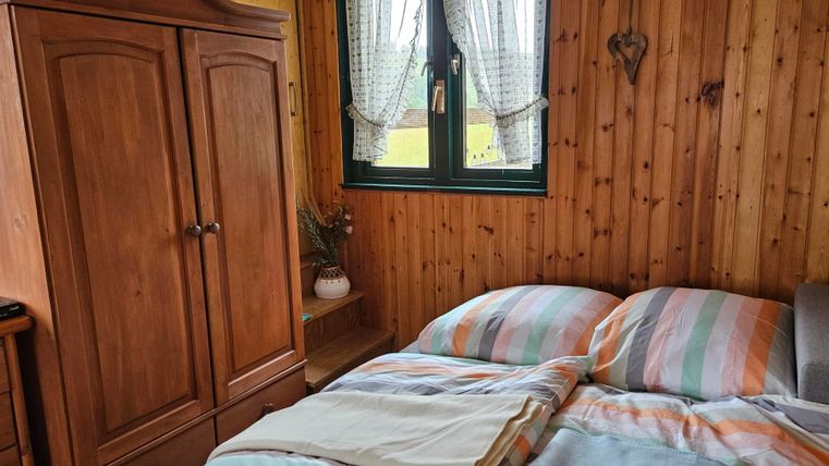 A cozy bedroom with wooden paneling and a large bed. A wardrobe and windows with curtains complete the space.
