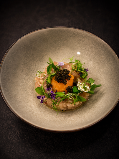 Een elegant gerecht in een witte kom, bestaande uit gehakt, een eidooier en verse kruiden. Gedeclareerd met kaviaar en eetbare bloemen.