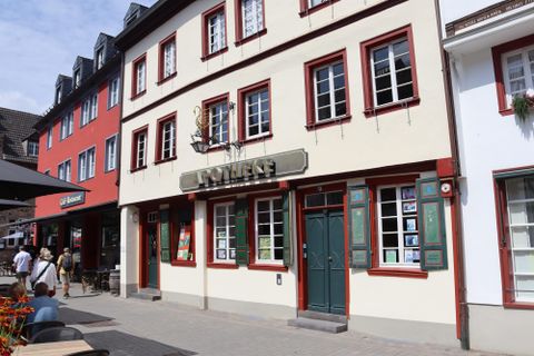 Un bâtiment historique avec l'inscription "Pharmacie". La façade est peinte en clair et a de nombreuses fenêtres avec des jardinières.