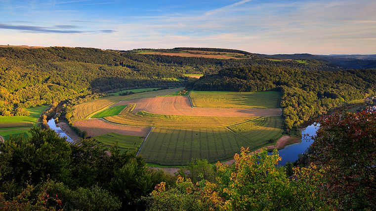 Paysage avec rivière, champs et forêts au coucher du soleil.