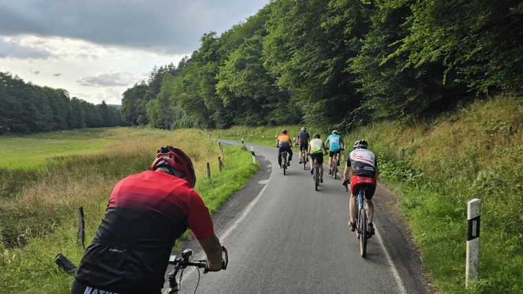 Groep fietsers op een landweg in de Eifel, omringd door groene weiden en bomen.