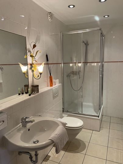 Een moderne badkamer met een douchecabine en een wastafel. De muren zijn betegeld en er is een stijlvolle verlichting.