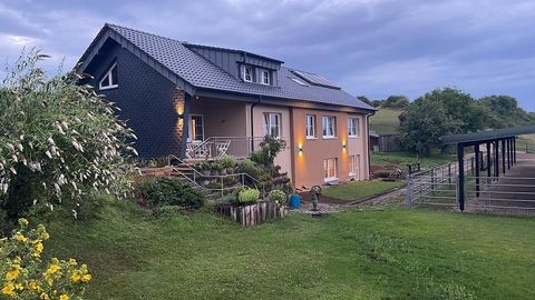Een mooi huis met een verzorgde tuin. Op de achtergrond zijn heuvelachtige weiden en een stal te zien.