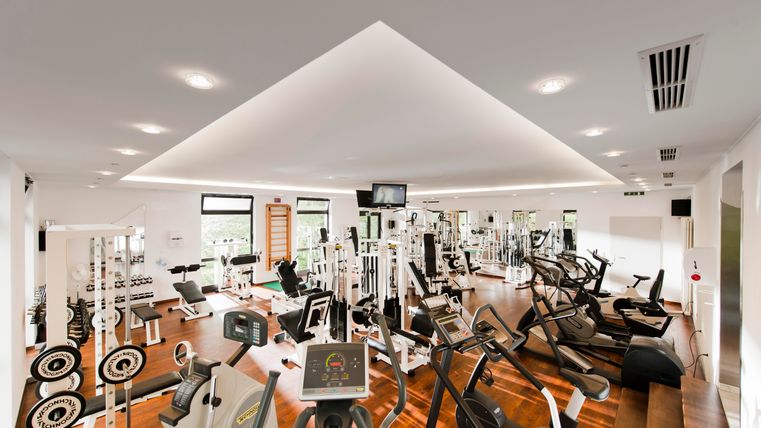 Een moderne sportschool met verschillende trainingsapparaten en een heldere, uitnodigende sfeer. De vloeren zijn van hout en er zijn grote ramen die veel licht binnenlaten.