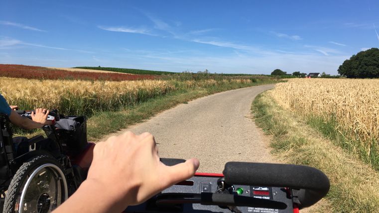 Person fährt mit Swiss Trac auf einem ländlichen Weg, umgeben von Feldern unter blauem Himmel.