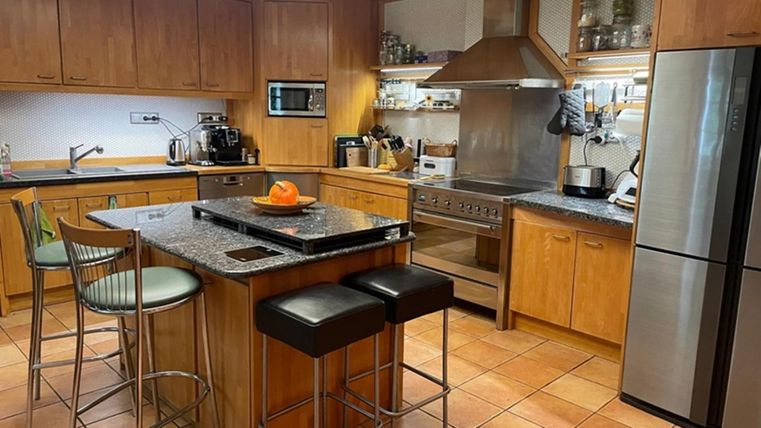 A modern kitchen with wooden furniture and granite surfaces. On the island, there is a bowl with an orange.