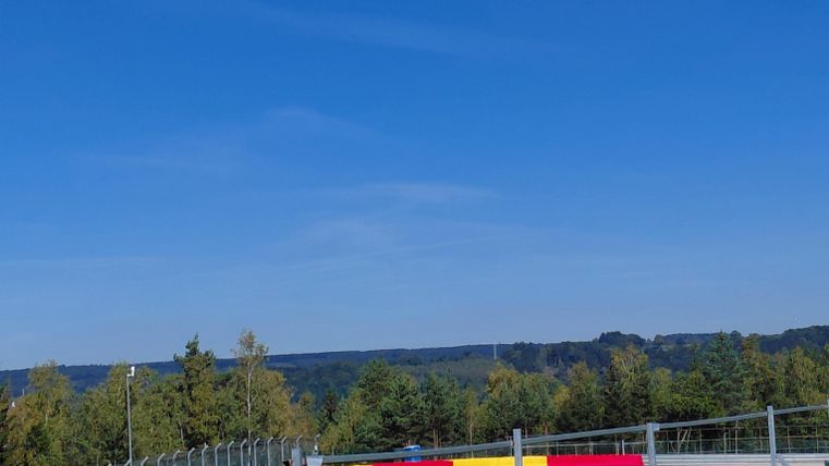 Une piste de course avec un ciel bleu clair. À l'arrière-plan, on peut voir des arbres et le paysage environnant.