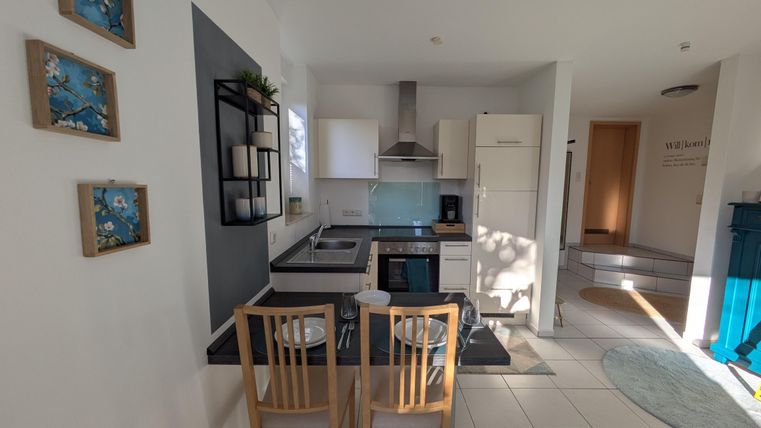 Een moderne keuken met lichte muren en witte meubels. Een eethoek met twee stoelen is naast de keukenkast te zien.