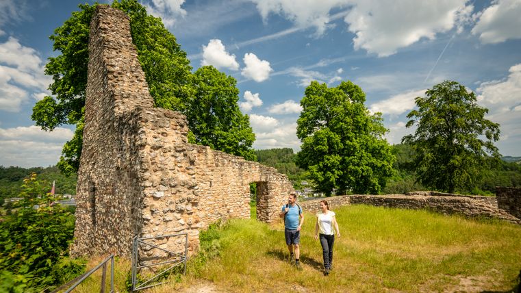 Deux personnes se promènent le long des ruines du Löwenburg à Gerolstein, entourées d'arbres verts et d'un ciel bleu.