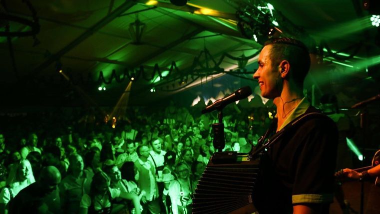 Een muzikant speelt op het podium voor een enthousiast publiek. De sfeer is levendig en verlicht met groene lichten.