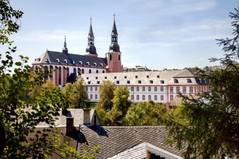 Een historisch klooster met twee markante torens. Omringd door bomen en een rustige omgeving.