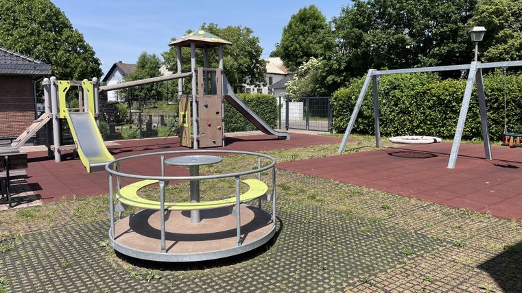 Frontalansicht auf die Spielgeräte, Kletterturm, Schaukel und Karussell.