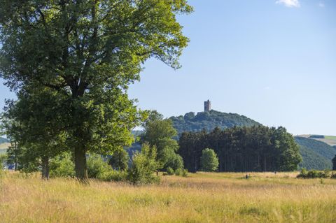 Un paysage idyllique avec un grand lac et des forêts environnantes. Au premier plan, des champs et un bâtiment sont visibles.