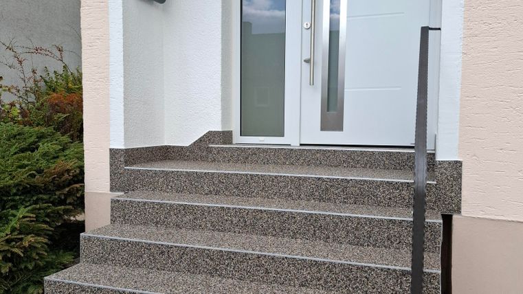 A modern entrance with steps and a glass front door. The surroundings are well-kept and inviting.