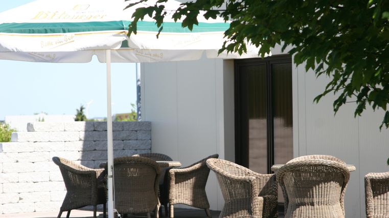 A cozy outdoor area with an awning and a table. Around the table are several woven chairs.