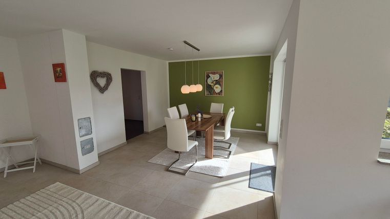 Une salle à manger moderne avec une table en bois et des chaises blanches. Les murs sont peints dans des couleurs douces et il y a beaucoup de lumière naturelle.
