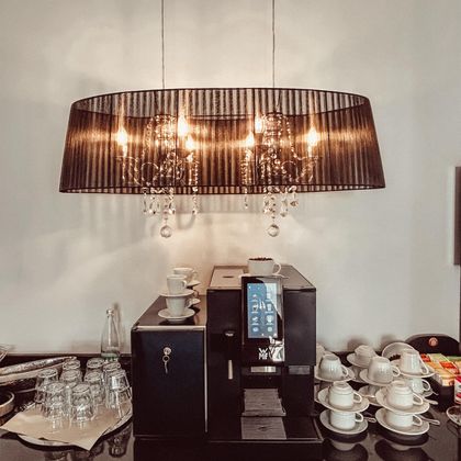 Une machine à café élégante se trouve sur une table sous une lampe au style raffiné. Autour, des verres et des tasses à café sont arrangés.