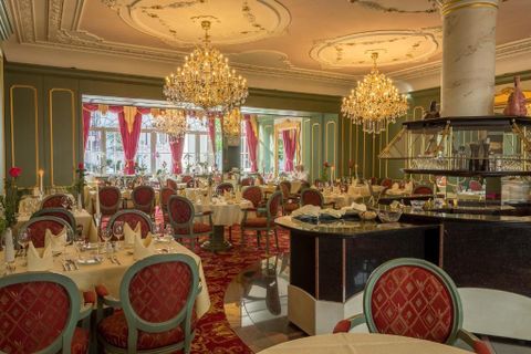 Een man in een zwarte mantel en een masker omarmt een vrouw met krullend haar die een elegante jurk draagt. In de hand van de man bevindt zich een kaarsenhouder met brandende kaarsen.