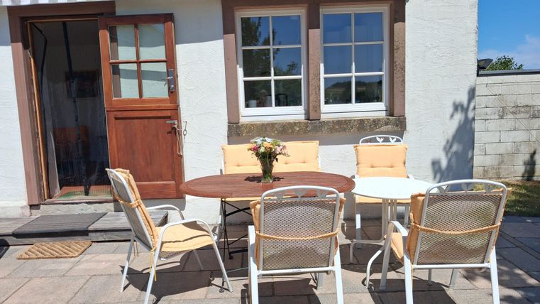 Un espace extérieur confortable avec une table et des chaises. Le soleil brille et il y a un centre de fleurs sur la table.