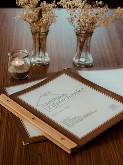 A wooden table with two menus and small vases with dried flowers. A candle creates a cozy atmosphere.