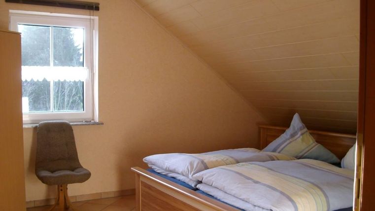 Een gezellige slaapkamer met schuine wanden. Het bevat een bed, een stoel en een raam met uitzicht naar buiten.