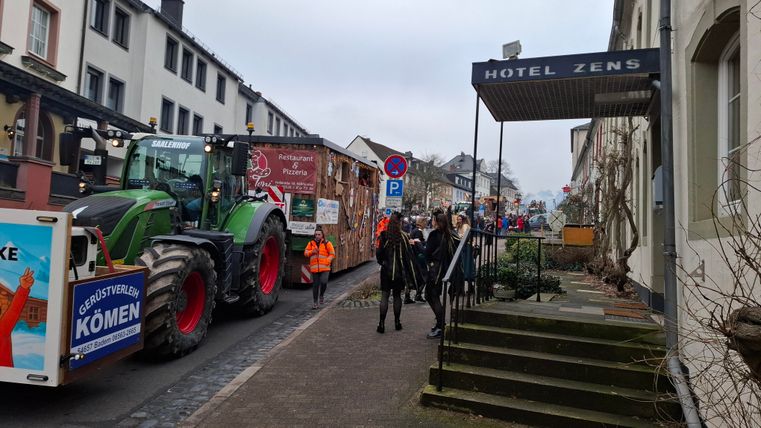 A street with a tractor and a festively decorated cart. People are standing on the sidewalk near the ZENS hotel.