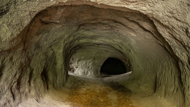 Binnenzicht van een natuurlijke grot met aarden muren en een donkere gang.