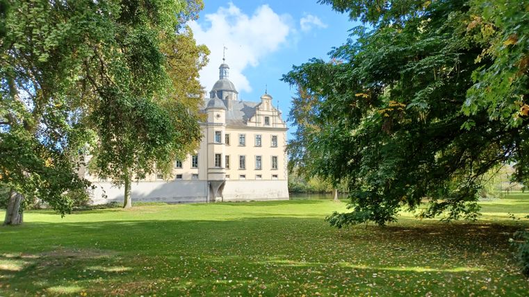 Kriegshoven Castle behind trees and lawn in sunny weather.