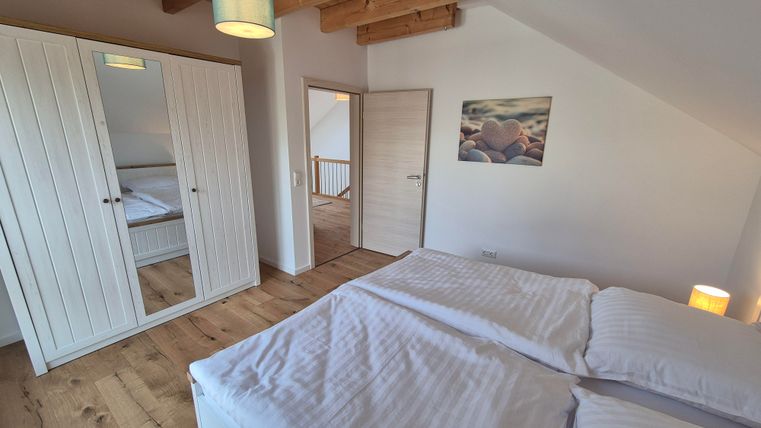 Une chambre claire avec deux lits et une grande armoire.
Des poutres au plafond et une belle image au mur créent une atmosphère agréable.