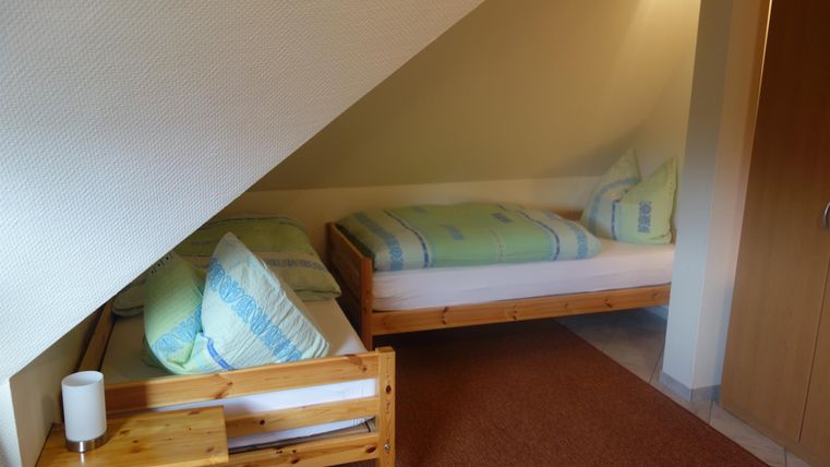 A cozy room with two beds and wooden-colored furniture. The walls are painted in soft colors.