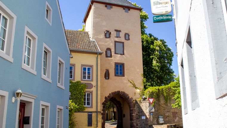 Historisches Stadttor in Dudeldorf mit angrenzenden Häusern und Straßenschild.