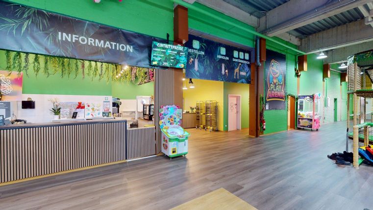 Een kleurrijke binnenruimte met een balie en speeltoestellen. De muren zijn groen geschilderd, en er zijn verschillende informatieschilderen.