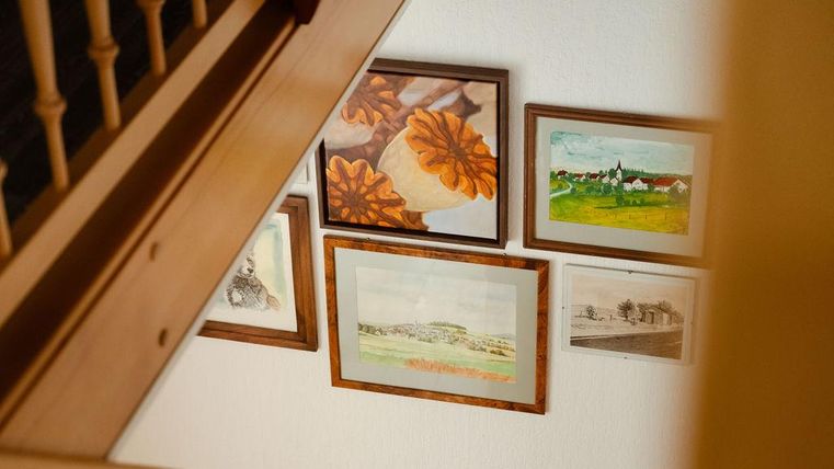 Une escalier qui montre plusieurs images au mur. Les images montrent entre autres la vue du village et des natures mortes dans des cadres.