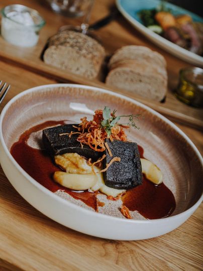 Een elegantere schotel met gebakken bloedworst, geserveerd op puree en een saus. Het gerecht is gegarneerd met knapperige uien en verse kruiden.