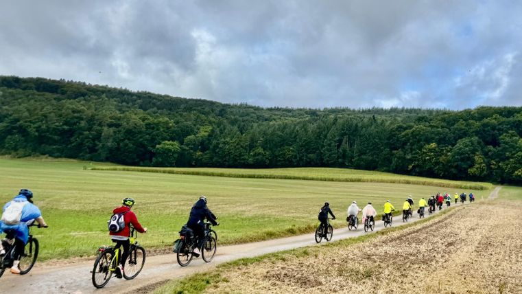 Vier mensen staan voor een café en poseren met een E-bike. Ze glimlachen en dragen sportieve kleding.