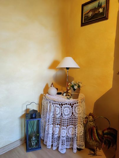 A cozy corner with a lace table and a lamp. Next to the table stands a lantern and a decorative rooster.