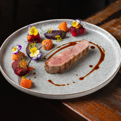 An artistically arranged plate with a piece of meat, garnished with colorful vegetables and edible flowers. The presentation looks elegant and appetizing.
