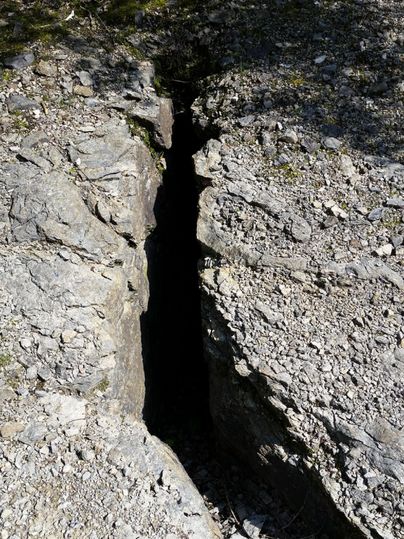 Une crevasse profonde dans la roche entourée de sol rocheux. L'image montre une impressionnante fente naturelle dans le paysage.