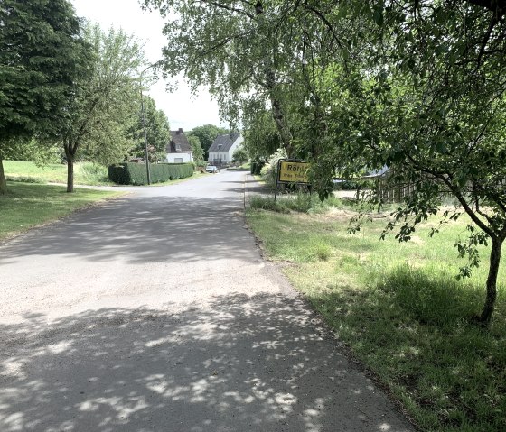 Straße in einem Dorf, gesäumt von Bäumen und einem Ortsschild 'Röhl'. Im Hintergrund sind Häuser zu sehen., © Benjamin Milbach