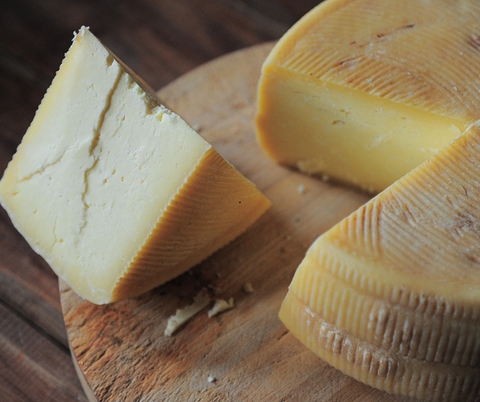 A large block of cheese has been cut and is resting on a wooden tray.