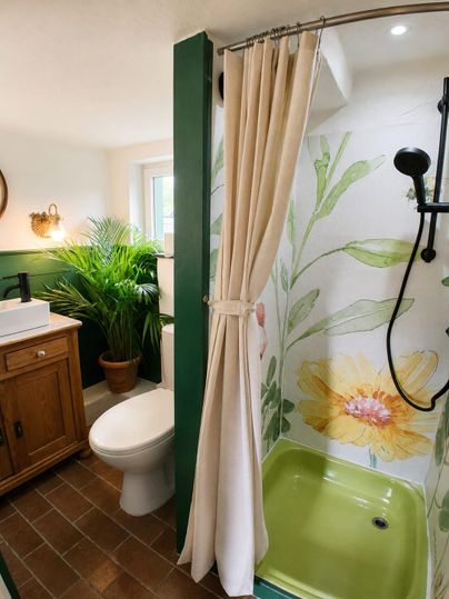 A modern bathroom with a shower and colorful wall paintings. In the background, there is a plant and a wooden cabinet.