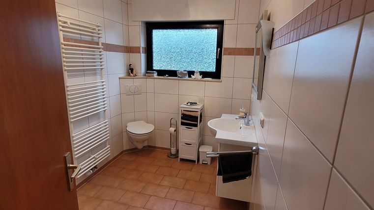 Ein modernes Badezimmer mit hellen Fliesen und einem Fenster. Es enthält eine Toilette, ein Waschbecken und einen Handtuchhalter.