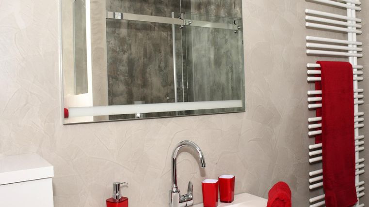 A modern bathroom with a white sink and a large mirror. Red towels and accessories add a color accent to the simple design.