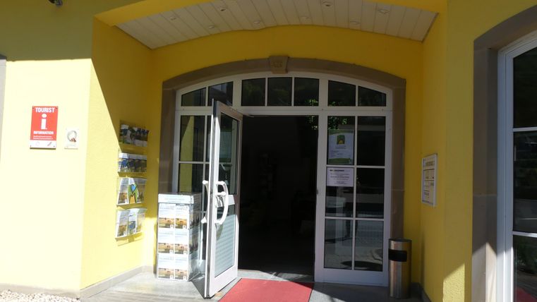 A bright entrance to a building with a yellow facade. The door is open and a red carpet leads inside.