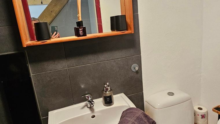 A modern bathroom with a sink and a large mirror. Towels in various colors are laid out on the shelf.
