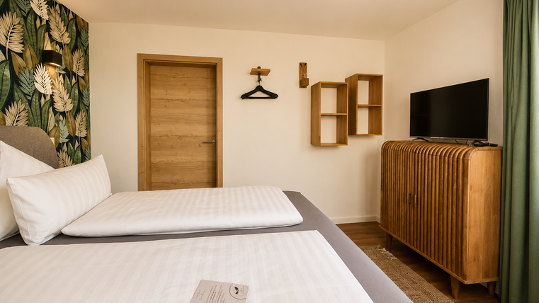 Een modern hotelkamer met twee bedden en een houten kast. De muren zijn versierd met een plantenmotief en er is een televisie en gordijnen in een zachte groentint.