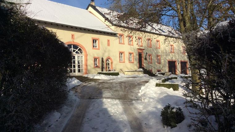 Ein charmantes Haus mit rotem Rahmen und einer schneebedeckten Einfahrt. Umgeben von grünen Büschen und Bäumen, strahlt es eine ruhige Atmosphäre aus.
