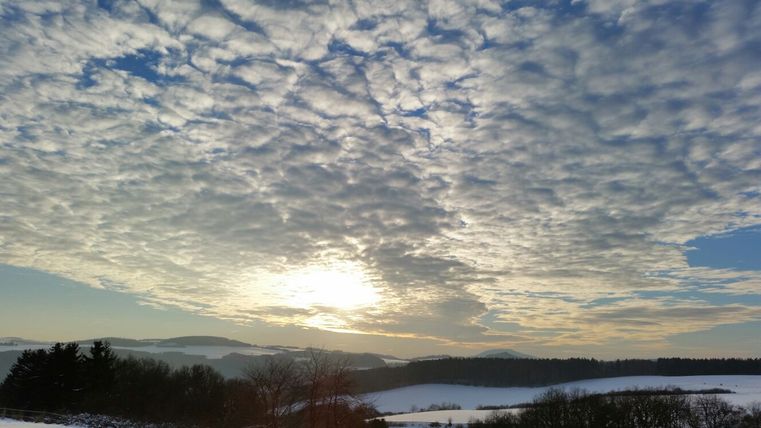 Winterlandschap in de Eifel met een bewolkte lucht en zonsondergang.